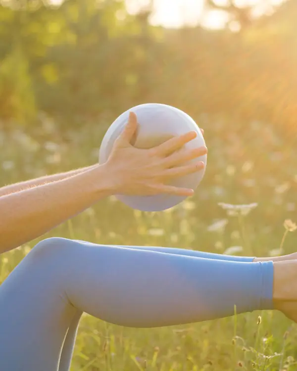 Close-up of a leg lift holding a Pilates ball, in light blue leggings